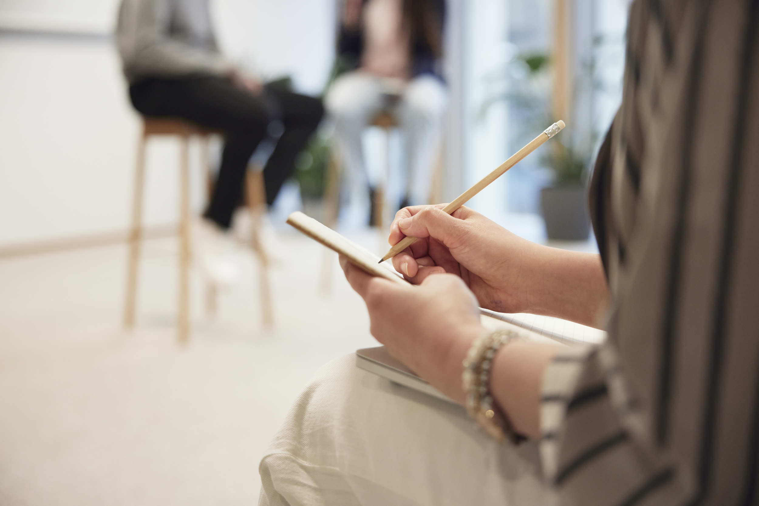 Person på föreläsning antecknar i block och två föreläsare